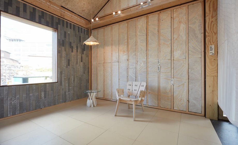 De muur met het raam is gebouwd met betonstenen van bacterien | The Exploded View Beyond Building, DDW21, ©About Today- BioLITH tiles made of bacteria and gravel by Biomason, insulation panels of mycelium by Grown.bio, floor tiles made of mycelium composite by Mogu, Terroir – Algae Paper Lamp by Jonas Edvard Studio, Tree table by Blast Studio and chair ‘Soof’ by Fabrikoos/ Anne Sophie Wouters